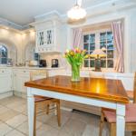 Küche mit Esstisch, Blumen und Fenster mit Vorhängen.