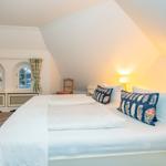 Schlafzimmer mit Dachschräge, zwei Fenstern und Bett mit Kissen.