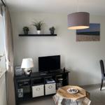 Wohnzimmer mit Fernseher, Couchtisch und Wandregal mit Pflanzen.