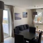 Wohn- und Essbereich mit Sofa, Tisch und Stühlen. Fenster und Balkontür mit Blick.