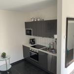 Küche mit grauen Schränken, Spüle und Kochfeld. Kleiner Tisch mit Pflanze daneben.