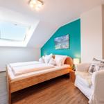 Doppelbett, Sessel, Dachs im Dachzimmer mit Dachfenster und blauer Wand.