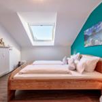 Schlafzimmer mit Dachschrägen, Holzbett und Dachfenster. Wand in Türkis mit Landschaftsbild.