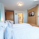 Schlafzimmer mit Bett, Fernseher und Holzwand