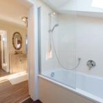 Bad mit Dusche und Badewanne, Blick in Wohnbereich mit Holzboden und Spiegel.