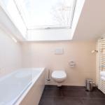 Badezimmer mit Dusche, Toilette und Waschbecken unter Dachfenster.