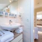 Badezimmer mit Waschbecken, Spiegel und Handtuchhalter. Blick in die Küche.