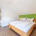 Schlafzimmer mit Doppelbett, grüner Wand und Holzmöbel.