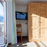 Ein Zimmer mit Holzschrank, Fernseher und Balkonblick auf Berge.