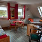 Wohnraum mit Sofa, Esstisch und Fenstern mit roten Vorhängen.