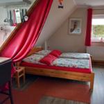 Schlafzimmer mit Dachschräge, roter Vorhang, Holzbett und Fenster mit Blick.