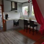 Küche mit Arbeitsplatte, Herd und Fenster. Zwei Barhocker stehen auf Teppich.