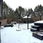 Schneebedeckter Garten mit Whirlpool, Pavillon und Holzhaus.