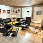 Wohnzimmer mit Ledersofa, zwei Sessel und Kaminofen. Holzfußboden und Wandbilder.