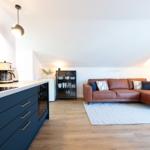 Wohn- und Küchenbereich mit braunem Sofa und dunkelblauen Schränken.