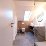 Badezimmer mit Dusche, Waschbecken und Toilette unter Dachschrägen.