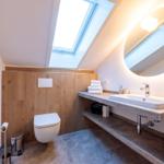 Badezimmer mit Dachschrägen, Waschbecken, Spiegel und Toilette.