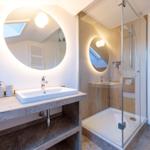 Badezimmer mit Dusche und Waschbecken unter runden Spiegel.