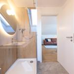 Badezimmer mit Dusche und Spiegel. Durchgang zum Wohnzimmer mit Sofa.