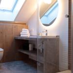 Badezimmer mit Duschabtrennung, Waschbecken und Toilette unter Dachschrägen.