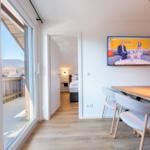 Wohnbereich mit Essplatz, TV und Blick auf Balkon mit Berglandschaft.