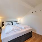 Schlafzimmer mit Doppelbett, Spiegel und Holzboden.