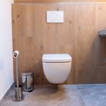Hängendes WC mit Wandbedienung, Holzwand und Handtüchern auf Regal