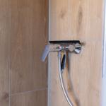 Duschbrause mit Handbrause und Chromarmatur an Holzfliesenwand.