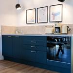 Küche mit blauen Schränken, Kaffeemaschine und Skiaufdrucken an der Wand.