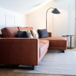 Ein Wohnzimmer mit braunem Sofa, Teppich und Stehlampe.