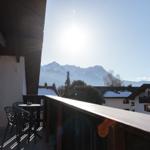 Terrasse mit Tisch und Stühlen, Blick auf schneebedeckte Berge und Dächer.