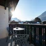 Balcony with table and chairs overlooking snowy mountains and rooftops.