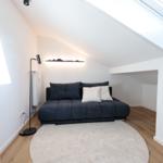Schlafzimmer mit Dachschrägen, Sofa, Teppich und Dachfenster.