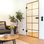 Wohnzimmer mit Sofa, Tisch und Pflanze. Tür mit Glasfeldern führt in den Flur.