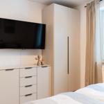 Schlafzimmer mit Bett, TV und Kleiderschrank. Fenster mit Vorhängen.