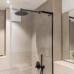 Dusche mit Glaswand, Duschbrause und Spiegel mit Pflanze.