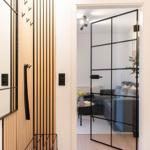 Eingangsbereich mit Holzvertäfelung und Glaswand zum Wohnzimmer mit Sofa und Tisch.