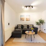 Ein Wohnzimmer mit grauem Sofa, Holztisch und Pflanze.