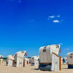 Weiß gestrichene Strandkörbe auf Sand unter blauem Himmel.