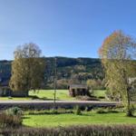 Haus mit Blick auf grüne Wiesen und bewaldete Berge unter blauem Himmel.