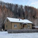 Ein Haus mit Schneebedecktem Dach und Holzveranda vor einem Wald.