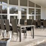 Terrace with tables and chairs under glass roof. Tile floor and planters.