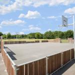 Basketball court with wooden fencing and hoop under blue sky.
