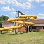 Yellow water slide in front of a building with a red roof.