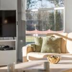 Living room with sofa, coffee table, and TV. Large windows with view of garden.