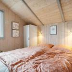 Bedroom with wooden walls, bed, and window. Bright lighting and wardrobes.