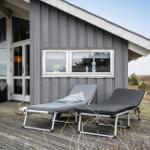 Deck with two lounge chairs in front of gray wooden house with windows.