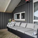 Terrace with sofa, table, and windows against gray wood wall.