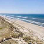 Aerial view of sandy beach with dunes and ocean waves.
