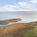 Aerial view of coastal wetlands with islands and calm water under a partly cloudy sky.
